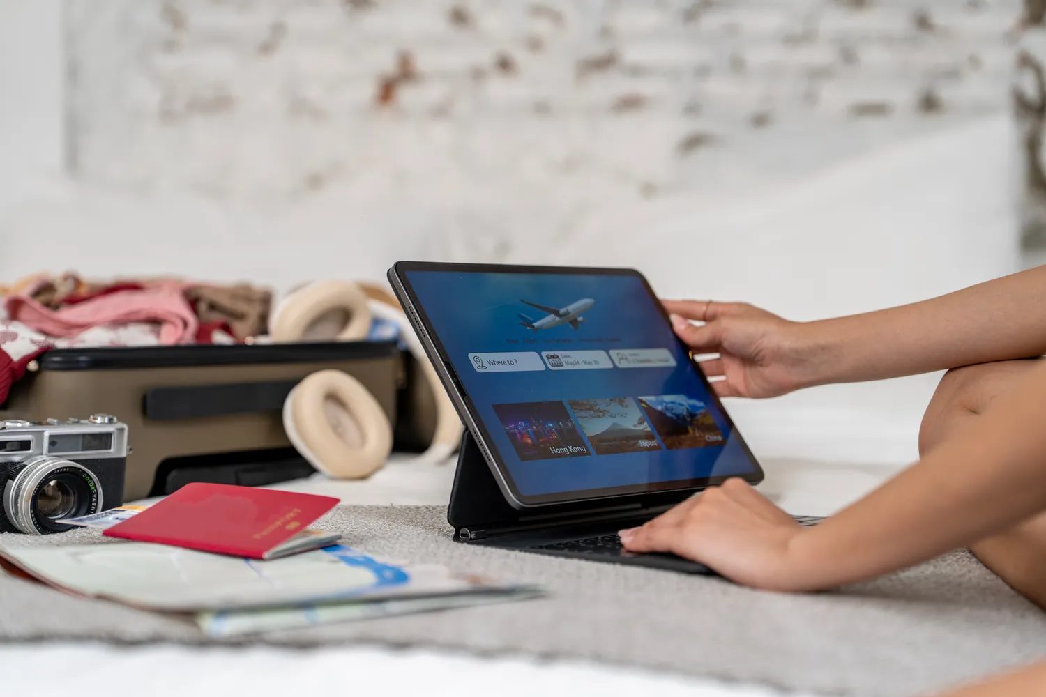 Traveler planning a trip on a tablet with an open suitcase and travel items nearby