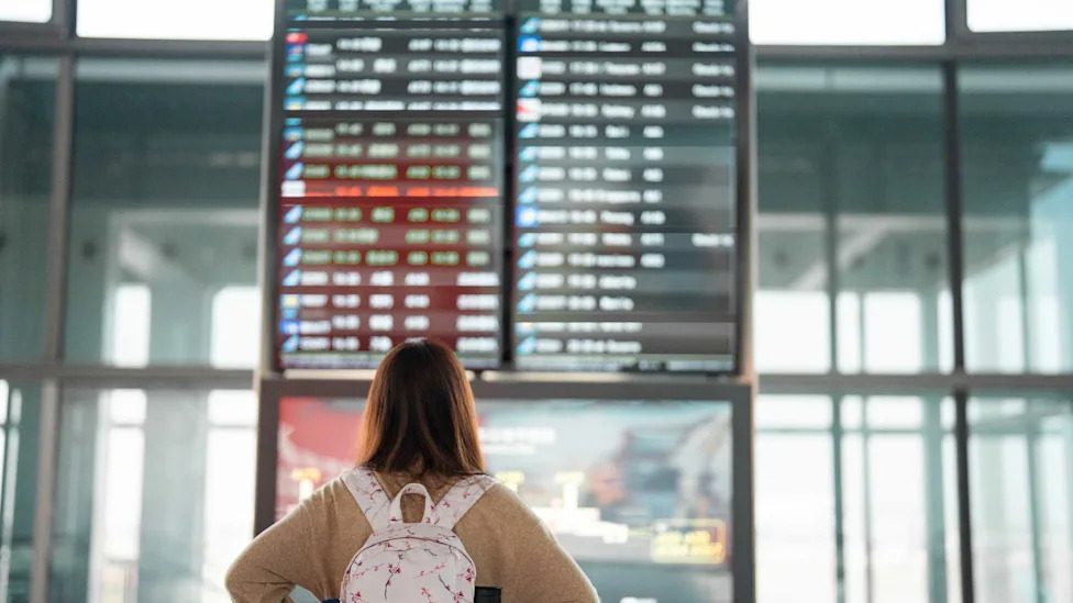 A woman looking at the flight schedule at an airport.