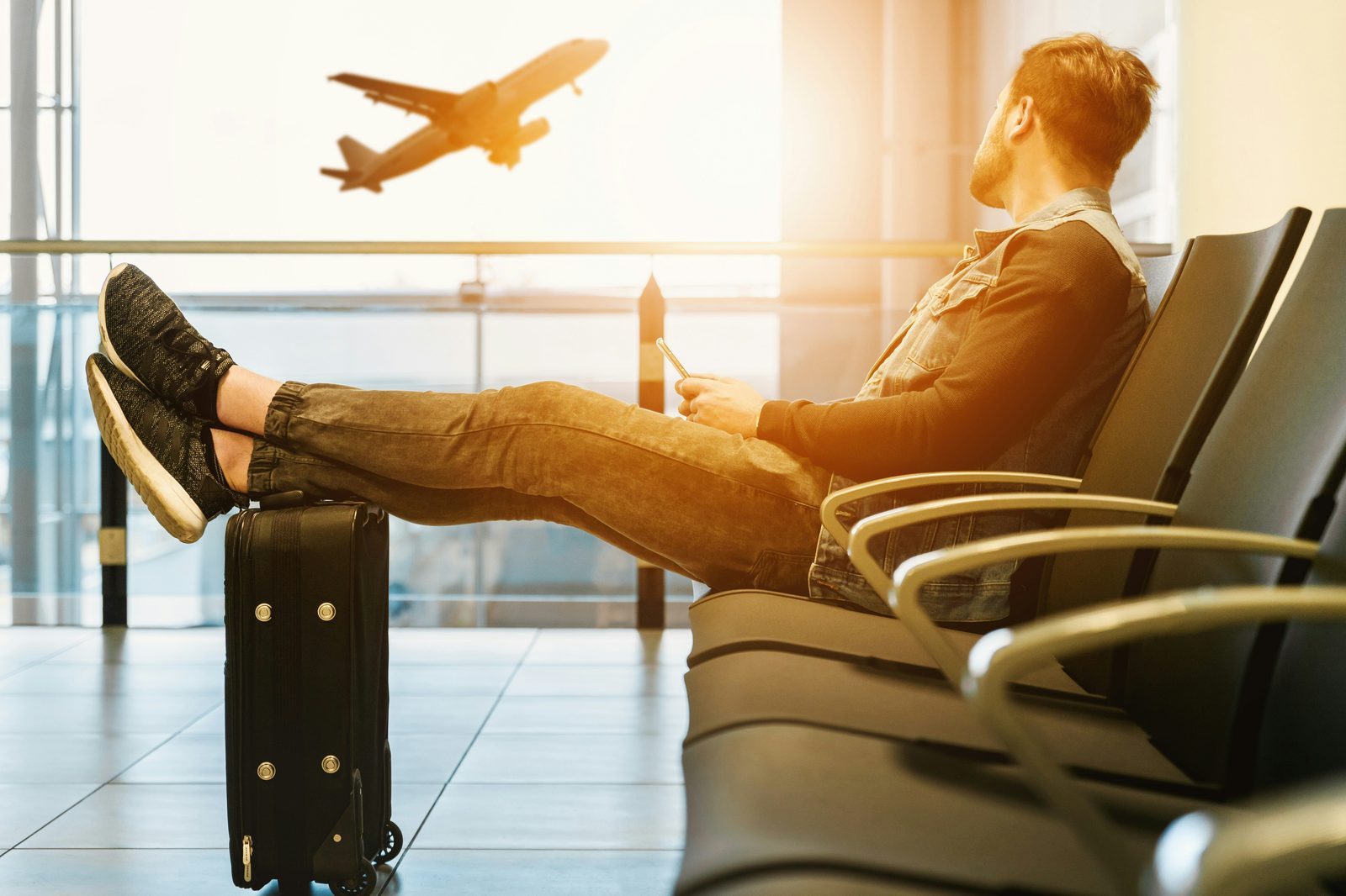 Traveller sitting in an airport with feet on luggage looking at an airplane