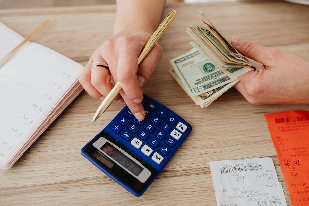 Person calculating vacation expenses with cash and a calculator on a desk