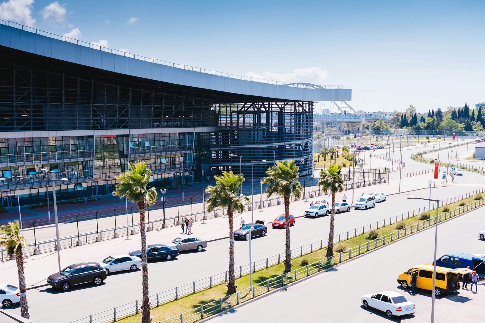 Vehicles travel along a road beside a large building, suggesting a location for airport price transfers.