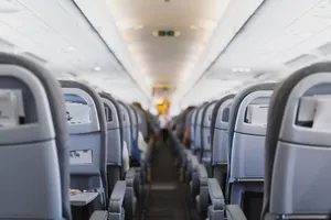 Rows of economy class airplane seats with seat backs featuring screens and storage pockets view down the aisle