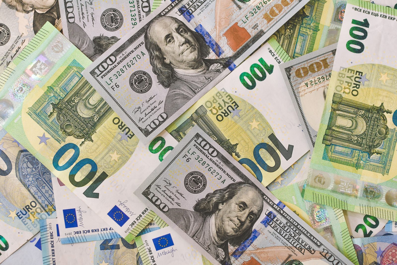 A pile of one hundred dollar bills and one hundred euro bills mixed together