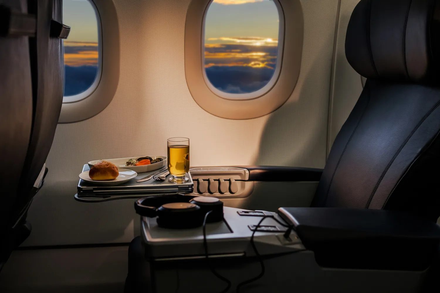 Airplane seat with meal tray on a table, sunset visible through the window