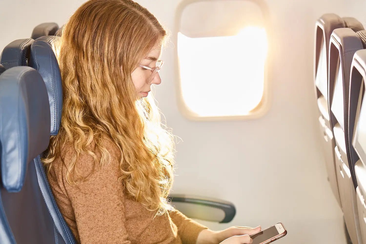A person seated on an airplane using a smartphone, managing a complex itinerary.