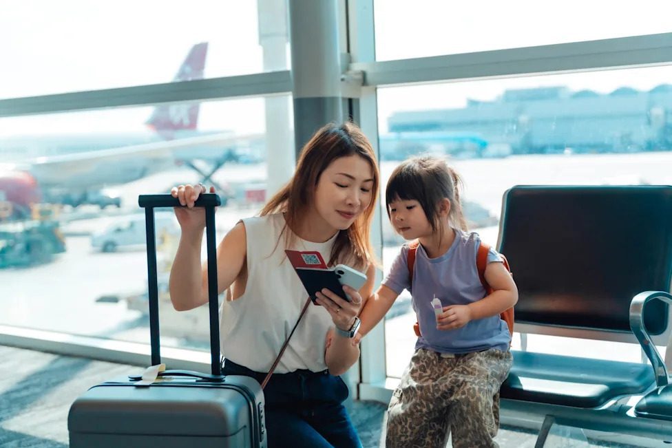 A woman and young girl in an airport together looking at a phone