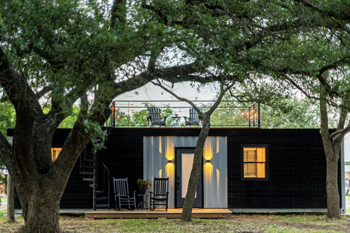 Cozy black tiny house with rooftop deck surrounded by trees at dusk