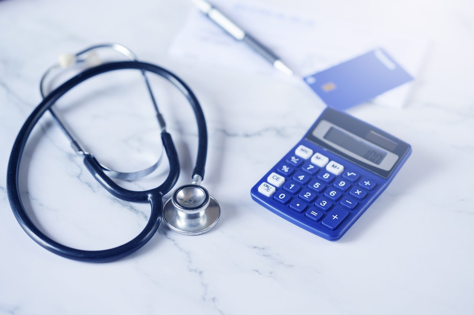 Stethoscope next to a credit card and calculator, symbolizing medical costs and budgeting