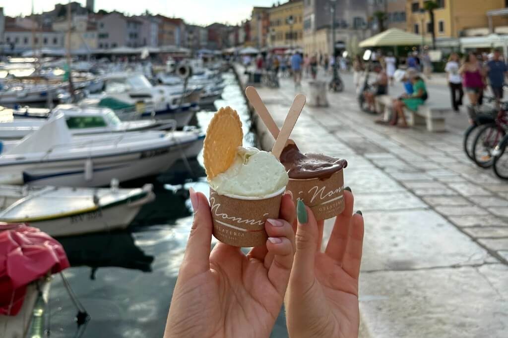 Two hands holding an ice cream in a cup in a colorful European harbor town
