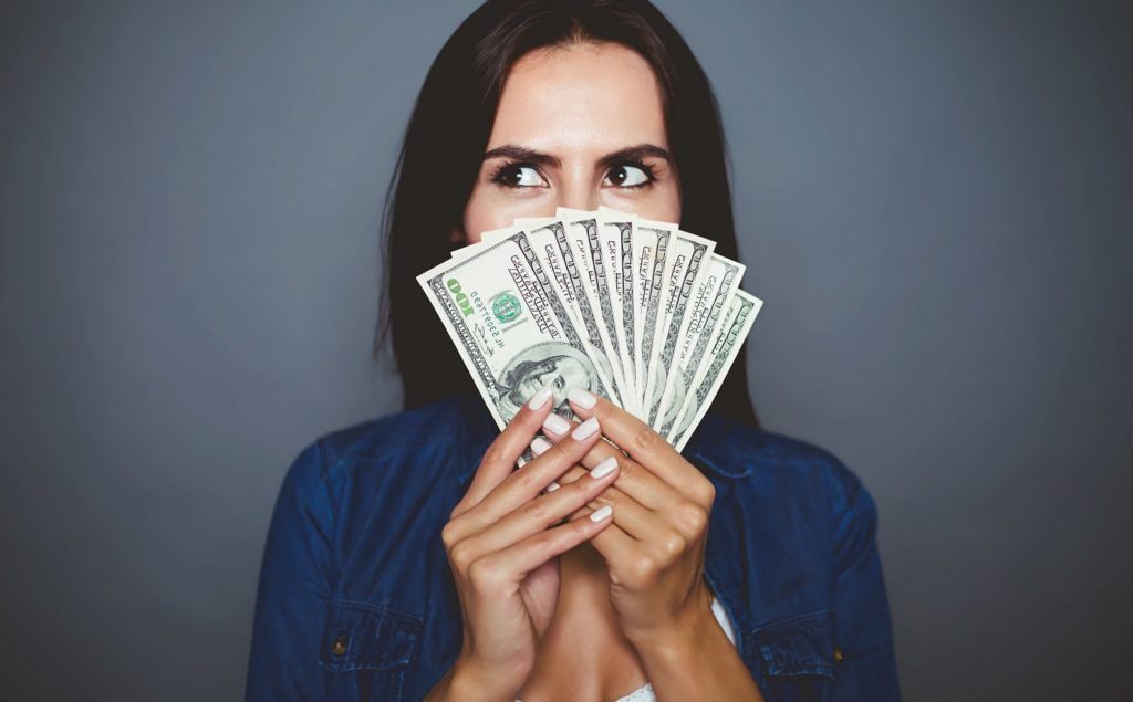 woman holding money - How To Save Money On Business Travel