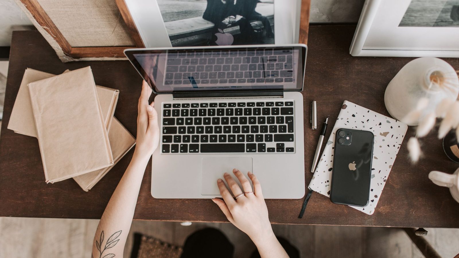 A top-down view of a person's hands on a laptop while planning travel with a phone and notebooks nearby.