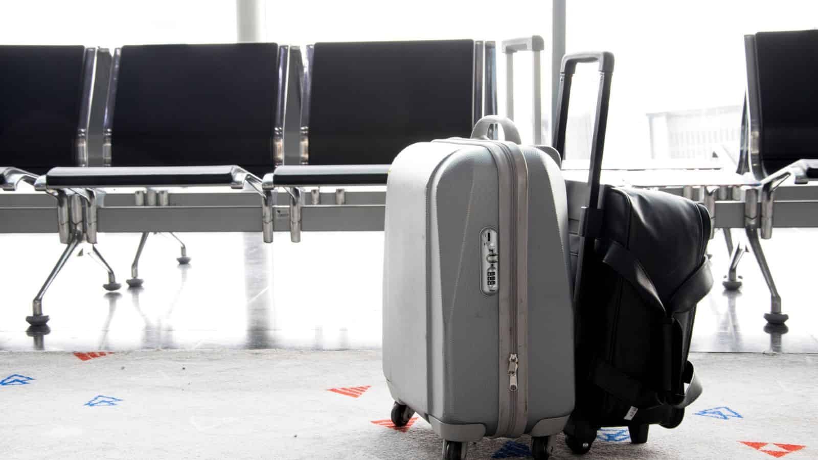 Two suitcases standing in an airport terminal with empty seats in the background