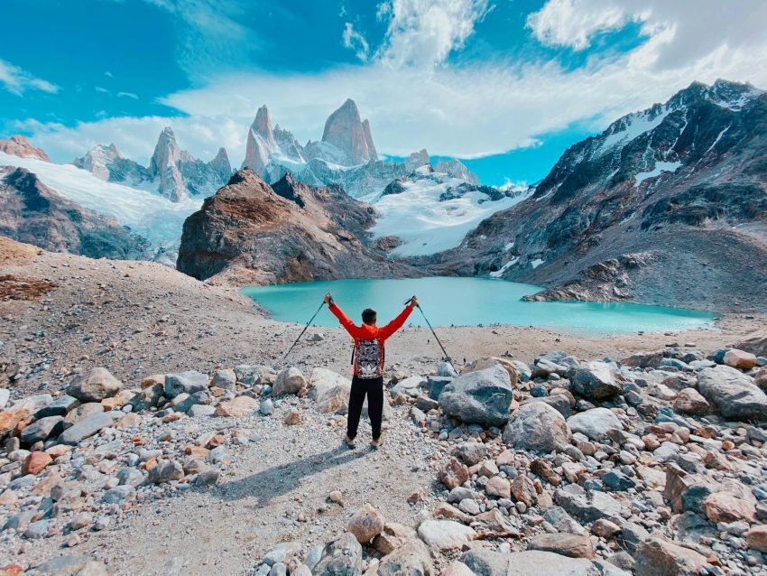 Traveler with arms raised in victory at Laguna de los Tres, Argentina, surrounded by mountains and a turquoise lagoon, symbolizing the payoff of thoughtful budgeting.