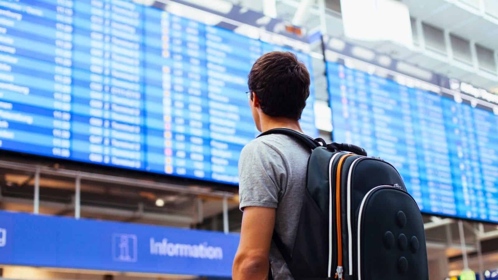 Traveler checking a large digital flight information board at an airport