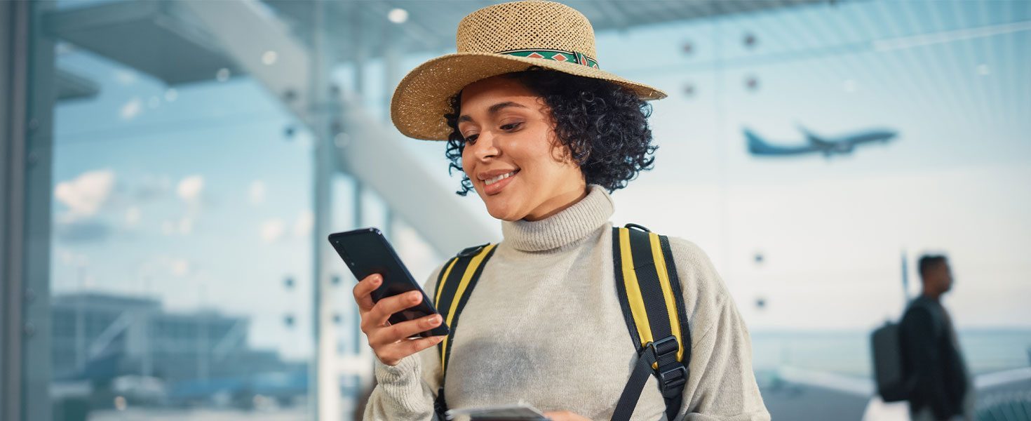 Woman using phone at airport with plane taking off behind her