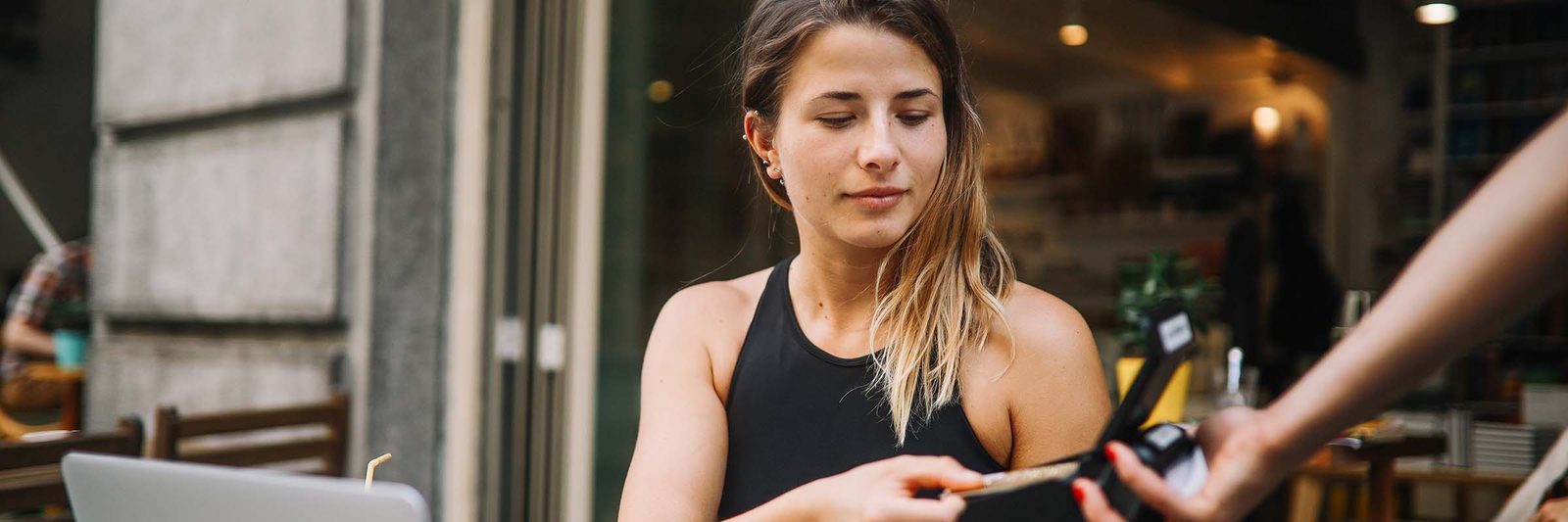 Young woman paying for coffee at a cafe, representing small but frequent post-trip expenses
