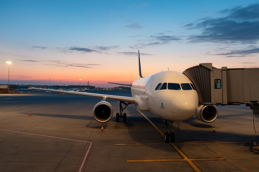 Passenger airplane parked at an airport gate during sunrise, with the boarding bridge connected and the sky showing early morning colors
