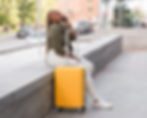 Traveler with a suitcase sitting on a bench, talking on the phone while sorting out last-minute accommodation