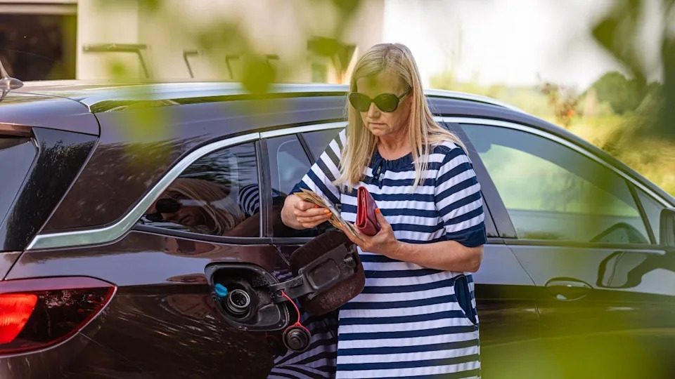 Woman holding euro cash near a car fuel tank during a stop at the pump