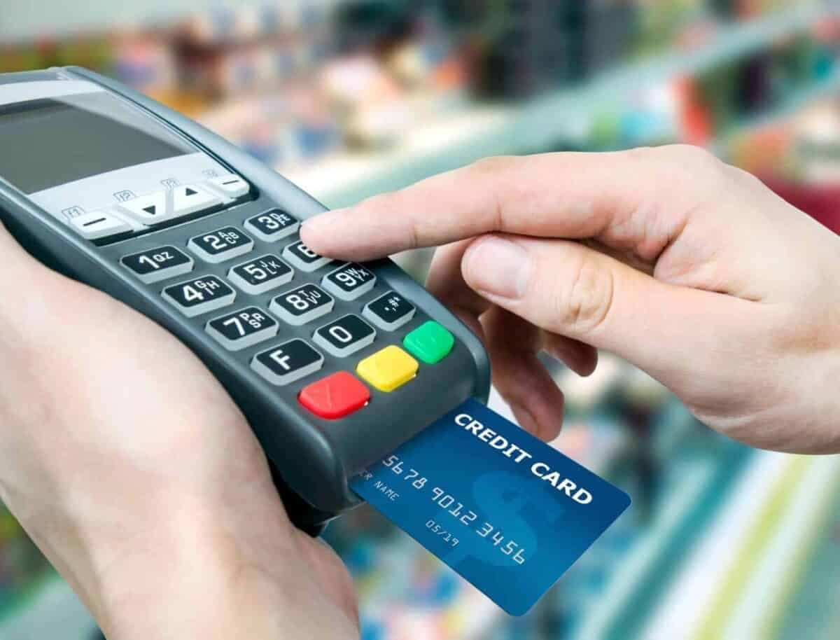 Hand holds a credit card terminal with a blue credit card in the chip reader.