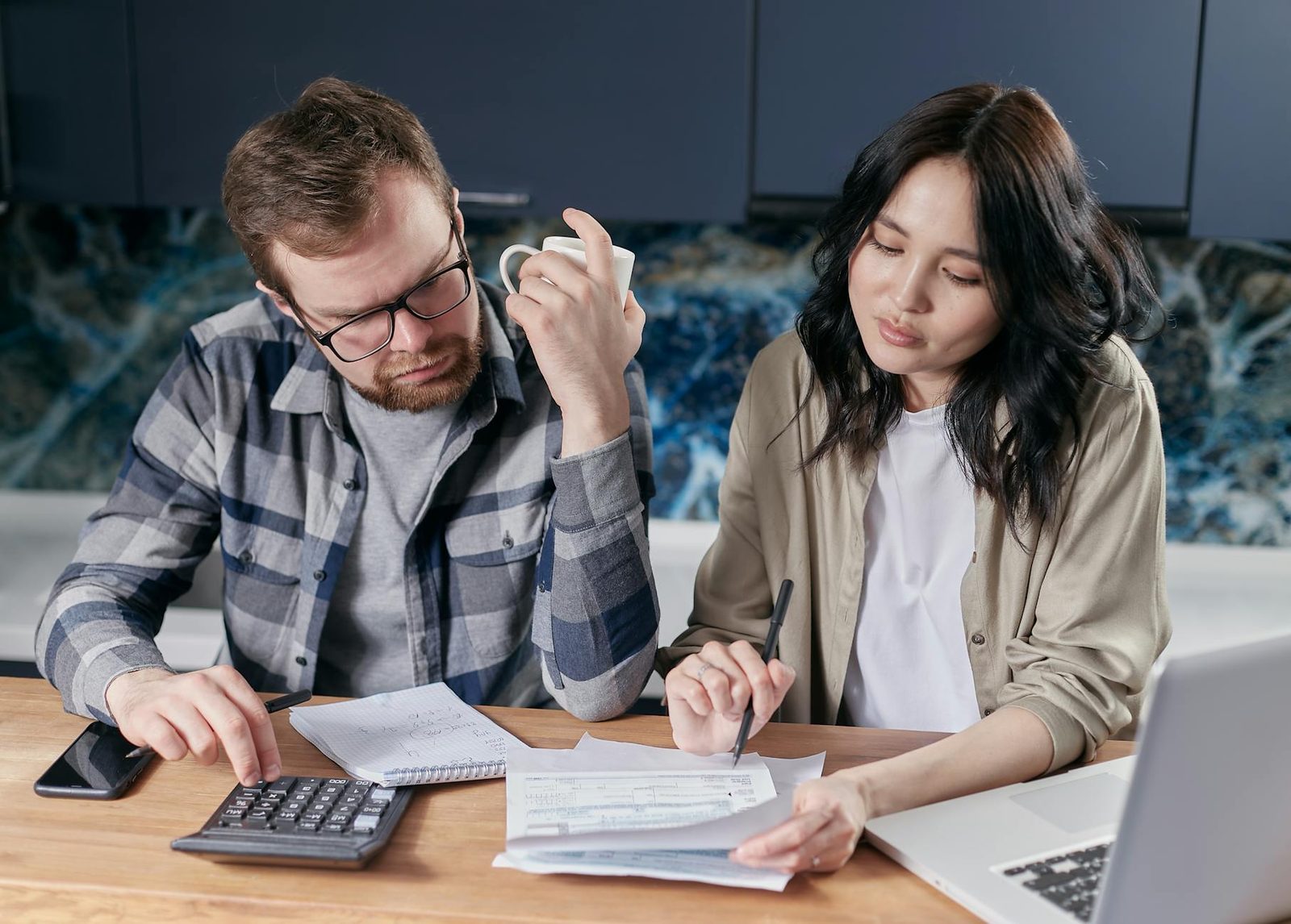 Couple reviewing vacation rental costs with calculator and laptop at kitchen table