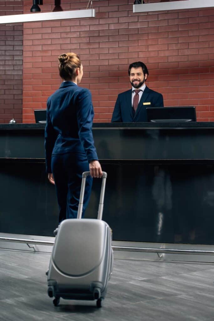 Woman with suitcase checking out at front desk of hotel before her flight departure