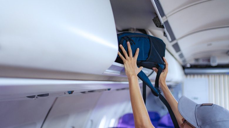 Person putting backpack in overhead compartment