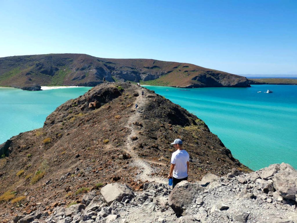 Traveler walking on rocks at a quiet bay in Mexico, illustrating how low-cost regions allow longer, slower, more relaxed trips.