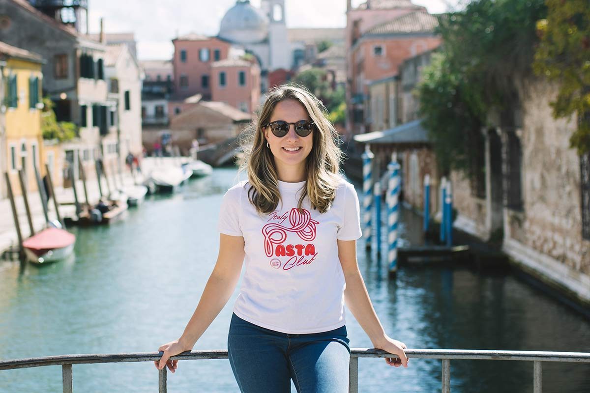 Tourists crossing a stone bridge over a Venetian canal on a sunny day, illustrating peak-time crowding in the historic center